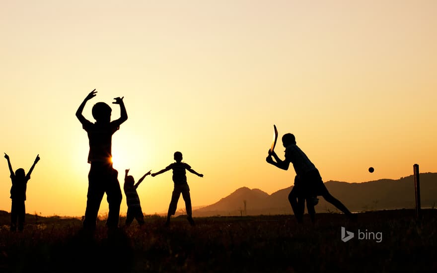 Silhouette of young Indian boys playing cricket against a sunset background